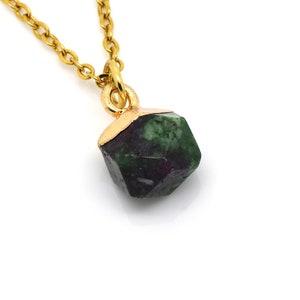 Peut inclure: Un collier en chaîne dorée avec un pendentif en pierre précieuse verte et violette. Le pendentif est facetté et a une forme géométrique.