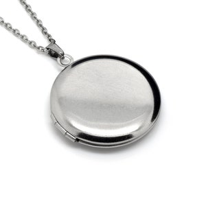 Op de afbeelding: Een zilveren ketting met een rond medaillon. Het medaillon is gesloten en heeft een glad, glanzend oppervlak.