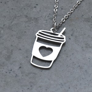 May include: A silver necklace with a pendant shaped like a coffee cup with a heart in the center. The cup has a straw sticking out of the top.