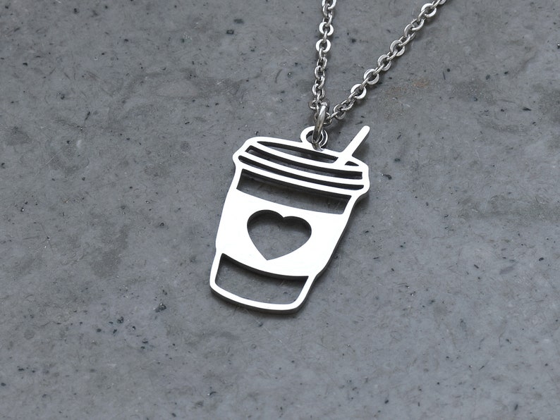 May include: A silver necklace with a pendant shaped like a coffee cup with a heart in the center. The cup has a straw sticking out of the top.