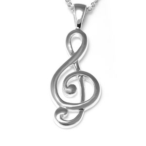 Peut inclure: Un collier avec un pendentif en argent en forme de clé de sol. Le pendentif est une représentation stylisée et détaillée d'une clé de sol.