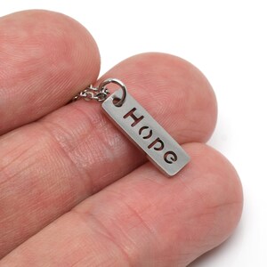 May include: A silver necklace with a small rectangular pendant that says "Hope" in a cut-out font.