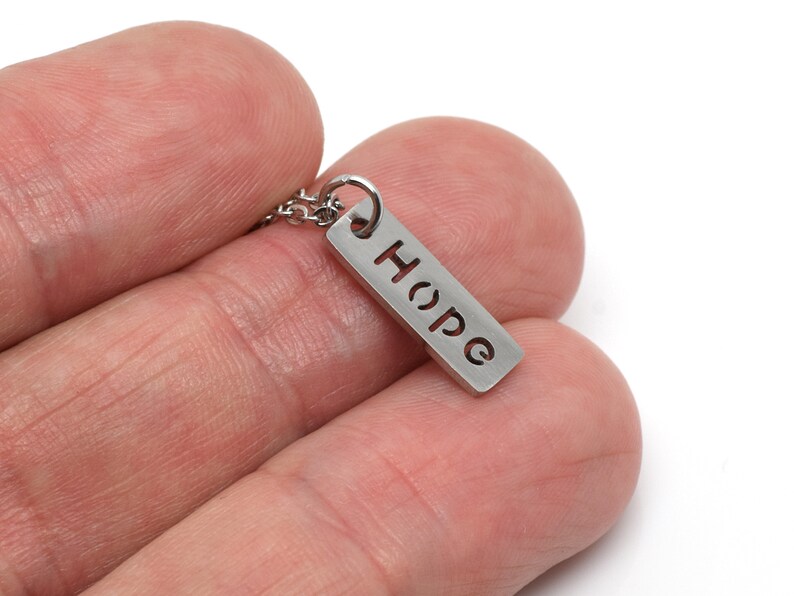 May include: A silver necklace with a small rectangular pendant that says "Hope" in a cut-out font.