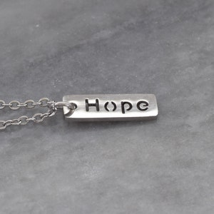May include: A silver necklace with a rectangular pendant that says "Hope" in a simple font.