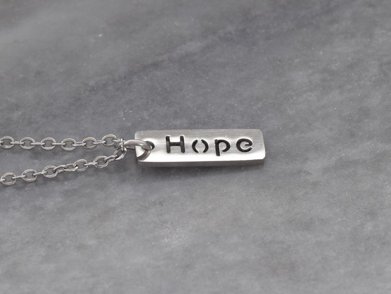 May include: A silver necklace with a rectangular pendant that says "Hope" in a simple font.