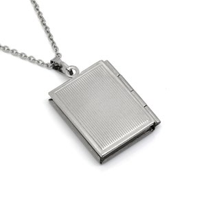 May include: A silver chain necklace with a silver locket pendant shaped like a book. The locket has a textured surface and a hinged closure.