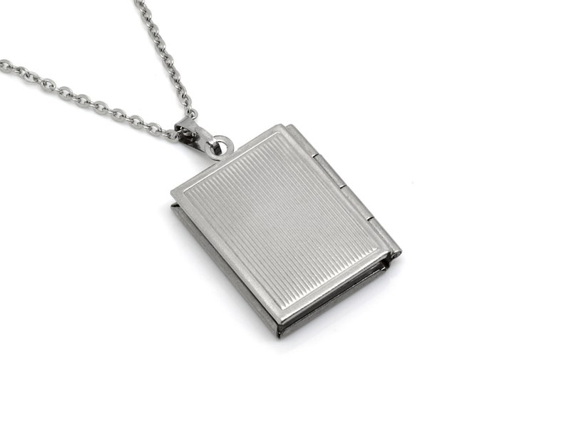 May include: A silver chain necklace with a silver locket pendant shaped like a book. The locket has a textured surface and a hinged closure.