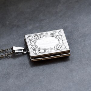 May include: A silver locket necklace with an ornate design and a hinged opening. The locket has a chain attached to it.