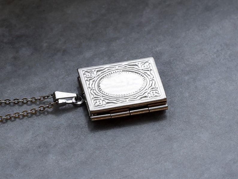 May include: A silver locket necklace with an ornate design and a hinged opening. The locket has a chain attached to it.