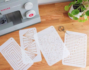 May include: Four white stencils with gold geometric designs on a wooden surface. The stencils are for crafting and decorating.  The designs include a series of triangles, a series of squares, a series of lines, and a series of fan-shaped designs.