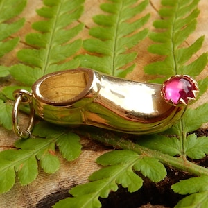 Puede incluir: Un amuleto de oro en forma de zapato con una piedra preciosa rosa en la punta.