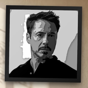 Pode incluir: Uma peça de arte de parede quadrada com um retrato gráfico em preto e branco de um homem com cabelo curto escuro e cavanhaque. O retrato é renderizado em tons contrastantes de cinza e preto, dentro de uma moldura preta simples.