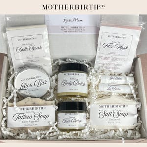 May include: A gift box filled with Motherbirth Co. bath and body products. The box contains a lotion bar, body polish, face polish, lip balm, bath soak, face mask, and soaps. The products are packaged in white and clear containers with black labels.