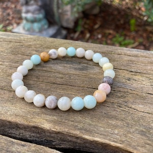 Puede incluir: Un brazalete hecho de cuentas de color verde claro, blanco y marr&oacute;n. Las cuentas son redondas y tienen un aspecto natural y pulido.