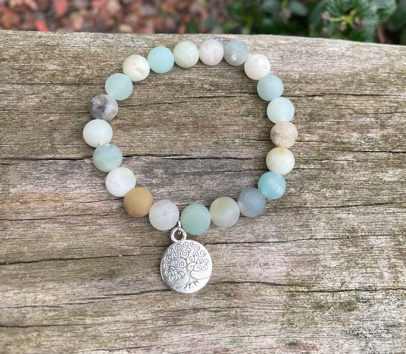 Puede incluir: Un brazalete de cuentas verdes, azules y marrones con un dije de plata de &aacute;rbol de la vida.