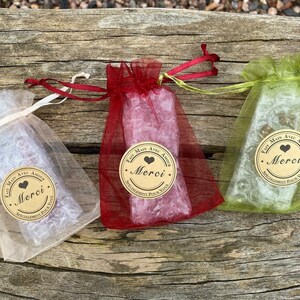 Puede incluir: Tres peque&ntilde;as bolsas de regalo hechas de tela transparente en rojo, verde y blanco. Cada bolsa tiene una etiqueta de papel marr&oacute;n con un coraz&oacute;n y el texto "Fait Main Avec Amour Merci. Specialement Pour Vous".