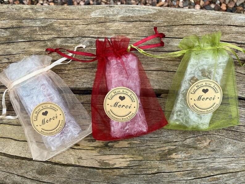 Puede incluir: Tres peque&ntilde;as bolsas de regalo hechas de tela transparente en rojo, verde y blanco. Cada bolsa tiene una etiqueta de papel marr&oacute;n con un coraz&oacute;n y el texto "Fait Main Avec Amour Merci. Specialement Pour Vous".