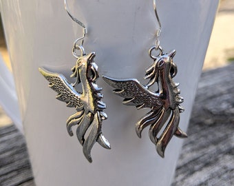 May include: A pair of silver earrings featuring a phoenix design. The phoenixes are facing upwards with their wings spread out.