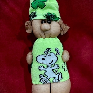 Może przedstawiać: Biały ceramiczny kubek z czarnym uchwytem i napisem "But First, Coffee" pogrubioną czcionką. Kubek jest umieszczony na rozmytym tle, sugerującym przytulne otoczenie.