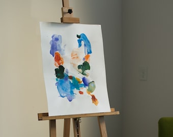 May include: A wooden easel with a white canvas displaying abstract watercolor art in shades of blue, green, orange, and purple.