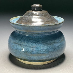 May include: A blue ceramic jar with a lid. The jar has a light blue glaze with darker blue streaks. The lid is dark gray with a small knob on top.