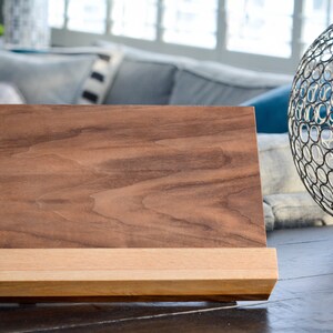 May include: A wooden book stand with a dark brown top and a light brown base. The stand is made of wood and has a simple design.