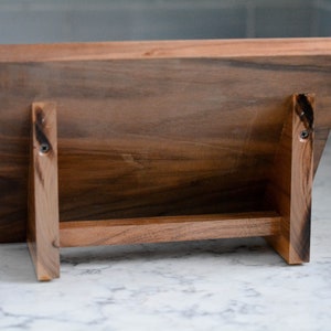 May include: A wooden chopping board with a stand. The board is made of dark wood and has a natural finish. The stand is made of the same wood and has a simple design.