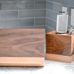 May include: A wooden kitchen utensil holder with a grater and a wooden chopping board.