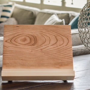 May include: A wooden book stand with a natural wood finish. The stand has a raised platform to hold a book or tablet.