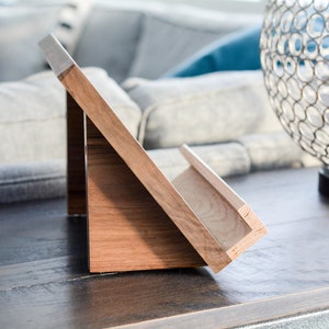 May include: A wooden book stand with a slanted surface and a shelf for holding books. The stand is made of light brown wood and has a natural finish.
