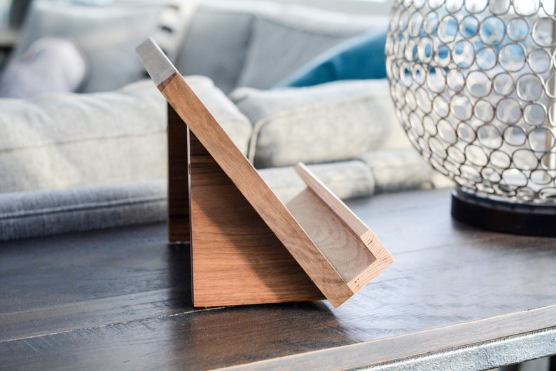 May include: A wooden book stand with a slanted surface and a shelf for holding books. The stand is made of light brown wood and has a natural finish.