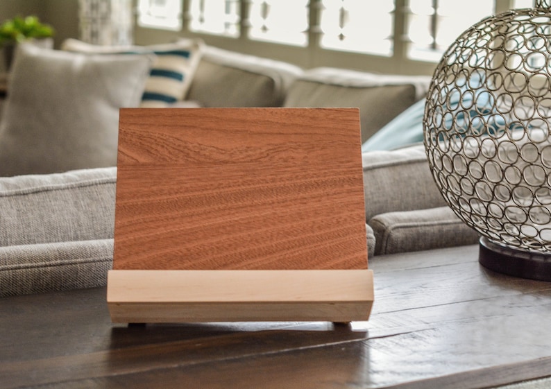May include: A wooden stand with a light brown base and a dark brown top. The stand is angled slightly forward and has a smooth, polished finish.