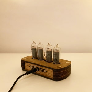 May include: A wooden clock with four clear glass tubes displaying the time. The clock is plugged in with a black cord. The clock is made of wood and has a dark brown finish.