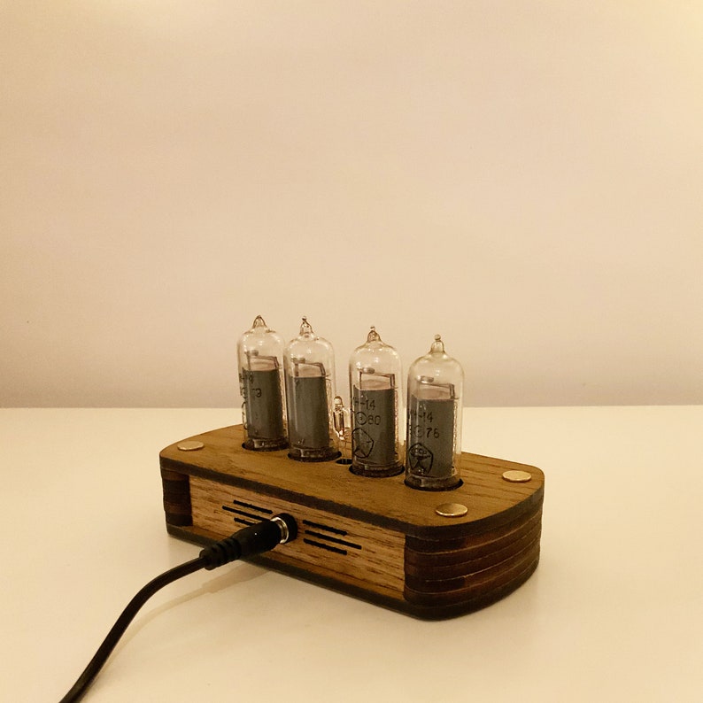 May include: A wooden clock with four clear glass tubes displaying the time. The clock is plugged in with a black cord. The clock is made of wood and has a dark brown finish.