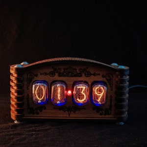 May include: A wooden digital clock with a decorative design. The clock displays the time "01:39" in glowing orange numerals within glass tubes. The wooden frame has a dark brown finish with blue LED lights.