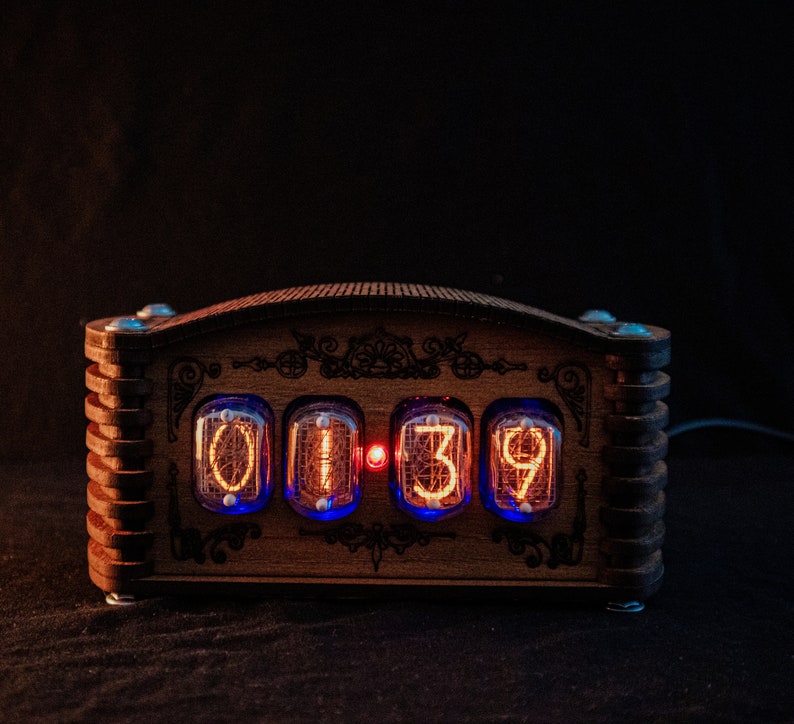 May include: A wooden digital clock with a decorative design. The clock displays the time "01:39" in glowing orange numerals within glass tubes. The wooden frame has a dark brown finish with blue LED lights.
