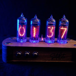 May include: A wooden clock with four glowing red Nixie tubes displaying the time 01:37. The clock has three knobs on the front and the text "Studio 77" is engraved on the wood.