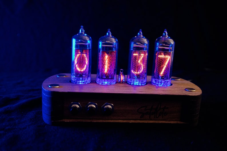 May include: A wooden clock with four glowing red Nixie tubes displaying the time 01:37. The clock has three knobs on the front and the text "Studio 77" is engraved on the wood.