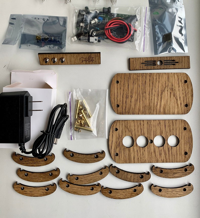 May include: A wooden kit for building a custom game console. The kit includes a variety of wooden pieces, including a top and bottom panel, buttons, and a control panel. The kit also includes a small bag of gold-colored screws and a small circuit board.
