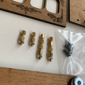 May include: Wooden electrical outlet covers with decorative etched designs. The image also shows brass standoffs, nuts, and small black components in a clear plastic bag. The wood has a natural grain.