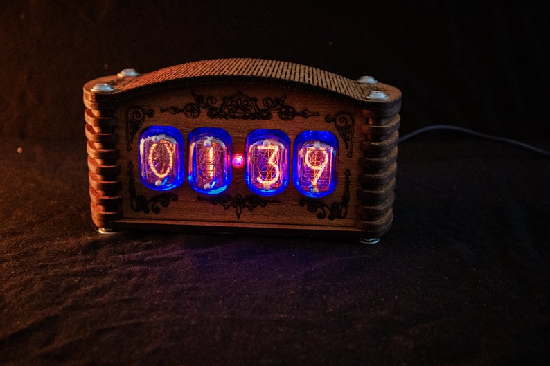 May include: A wooden digital clock with four glowing orange digits, displaying "0139". The clock has a decorative wooden frame with ornate details and blue neon lighting around the numbers. The clock is on a dark surface.