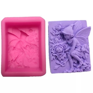 May include: A pink silicone mold with a floral design and a purple silicone mold with a fairy design. The fairy is sitting on a branch with wings spread and holding a flower.