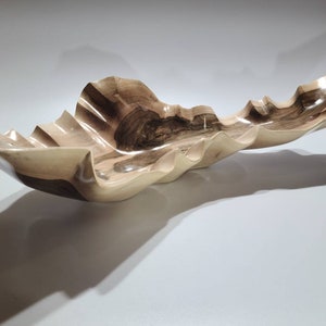 May include: A large, wooden bowl with a wavy, organic shape. The bowl is made of light brown wood with dark brown streaks. It is a unique and decorative piece.