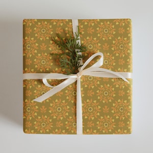 May include: A gift box wrapped in green and orange patterned paper with a white ribbon and a sprig of greenery on top.