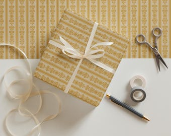 May include: A gift wrapped in yellow and white patterned paper with a white ribbon. The gift is on a white surface with a roll of tape, a pen, and scissors.