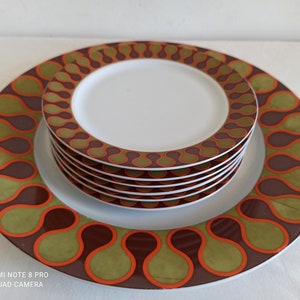 Può includere: Un set di piatti in ceramica bianca con un design retrò. I piatti presentano un motivo marrone, arancione e verde sui bordi. Il set include un grande piatto da portata con un design coordinato. È visibile una pila di piatti più piccoli.