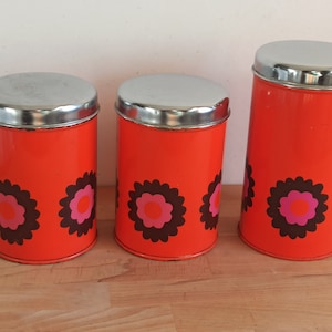Peut inclure: Ensemble de trois boîtes de conserve vintage en métal orange avec des couvercles argentés. Chaque boîte présente un motif floral marron, rose et orange. Les boîtes cylindriques varient en hauteur, pour un rangement de cuisine rétro.