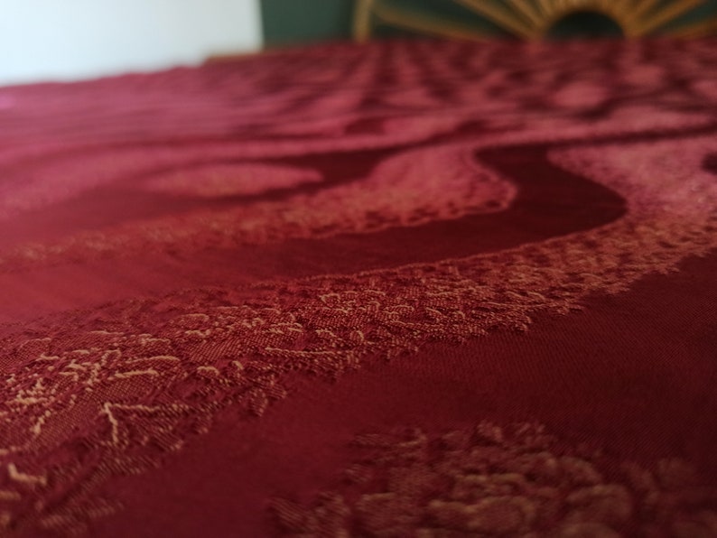 May include: Close-up of a deep red fabric with a swirling, textured pattern. The fabric has a subtle sheen and a detailed, raised design in a lighter shade of red, creating a sense of depth and luxury. The overall theme is textiles.