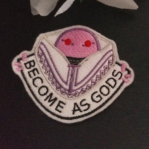 May include: Two white embroidered iron-on patches with pink cartoon faces and the text "Become as Gods".