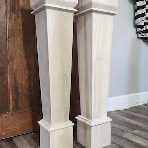 May include: Two unfinished wooden columns with a square top and base. The columns are light-colored and stand on a wood-look floor. The columns are approximately 40 inches tall.